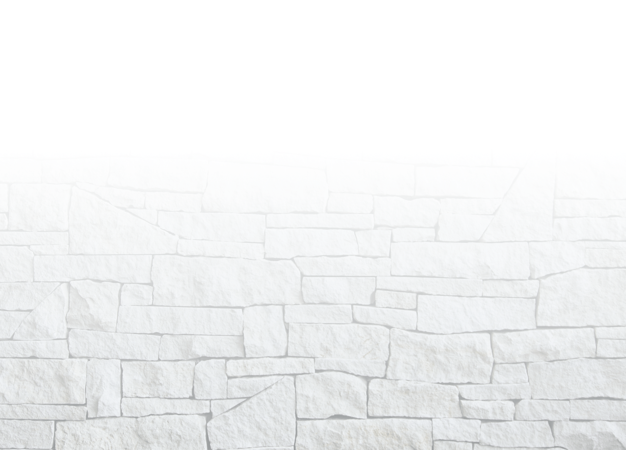 A textured, light-colored stone wall with irregular rectangular shapes, giving a rustic appearance against a bright, white background.