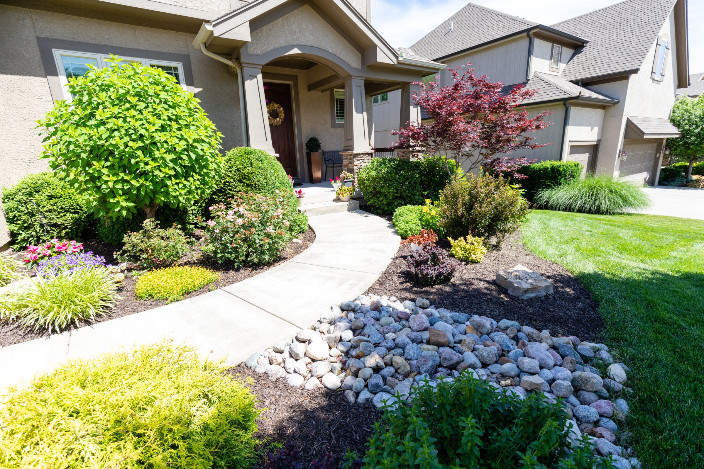 A suburban home with a beautifully landscaped front yard, featuring colorful flowers, shrubs, and a stone path leading to the front door.