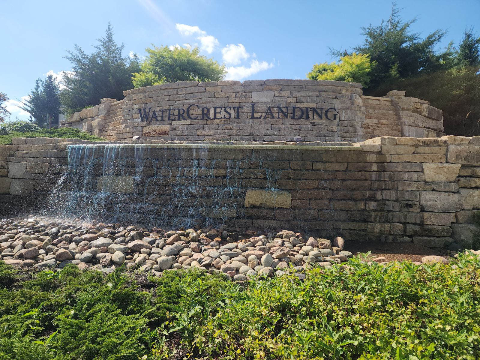 Stone structure labeled "WaterCrest Landing" with cascading waterfall, surrounded by rocks and lush greenery under a clear blue sky.