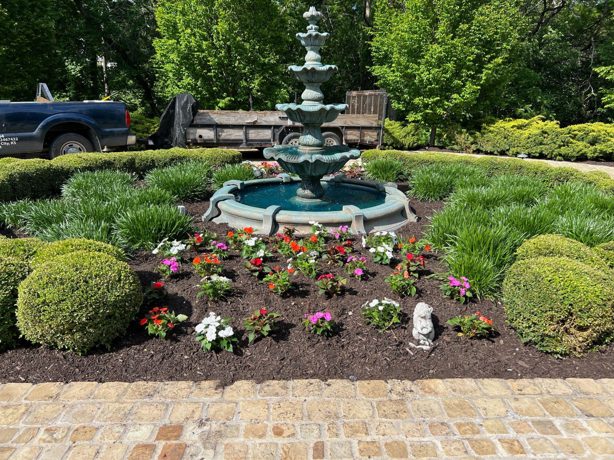 Decorative fountain surrounded by flowers and trimmed shrubs
