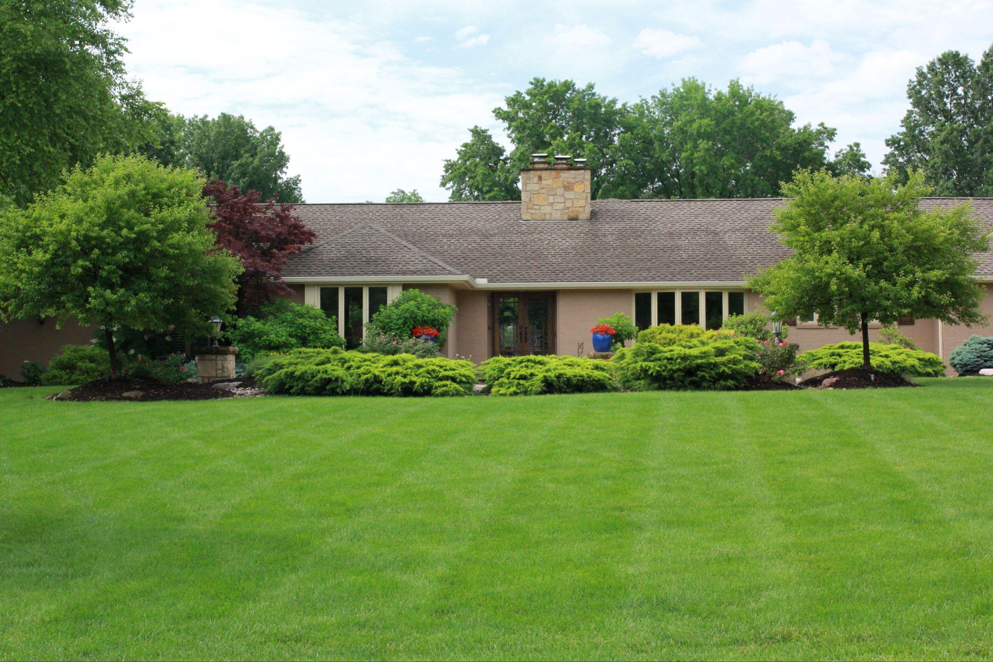 Front view of a single-story home with lush green lawn, manicured shrubs, and mature trees maintained with professional landscape maintenance services