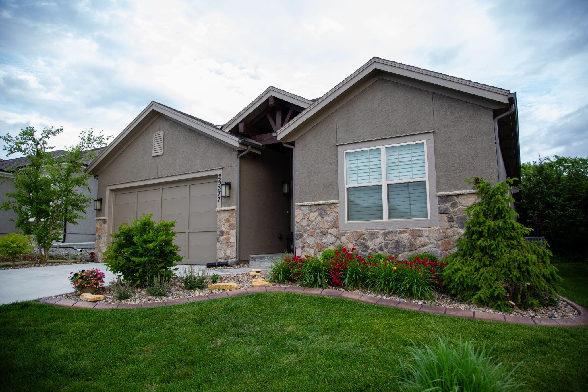 Front yard of a modern single-story home with manicured lawn, stone accents, curved landscape bed, and neatly trimmed shrubs