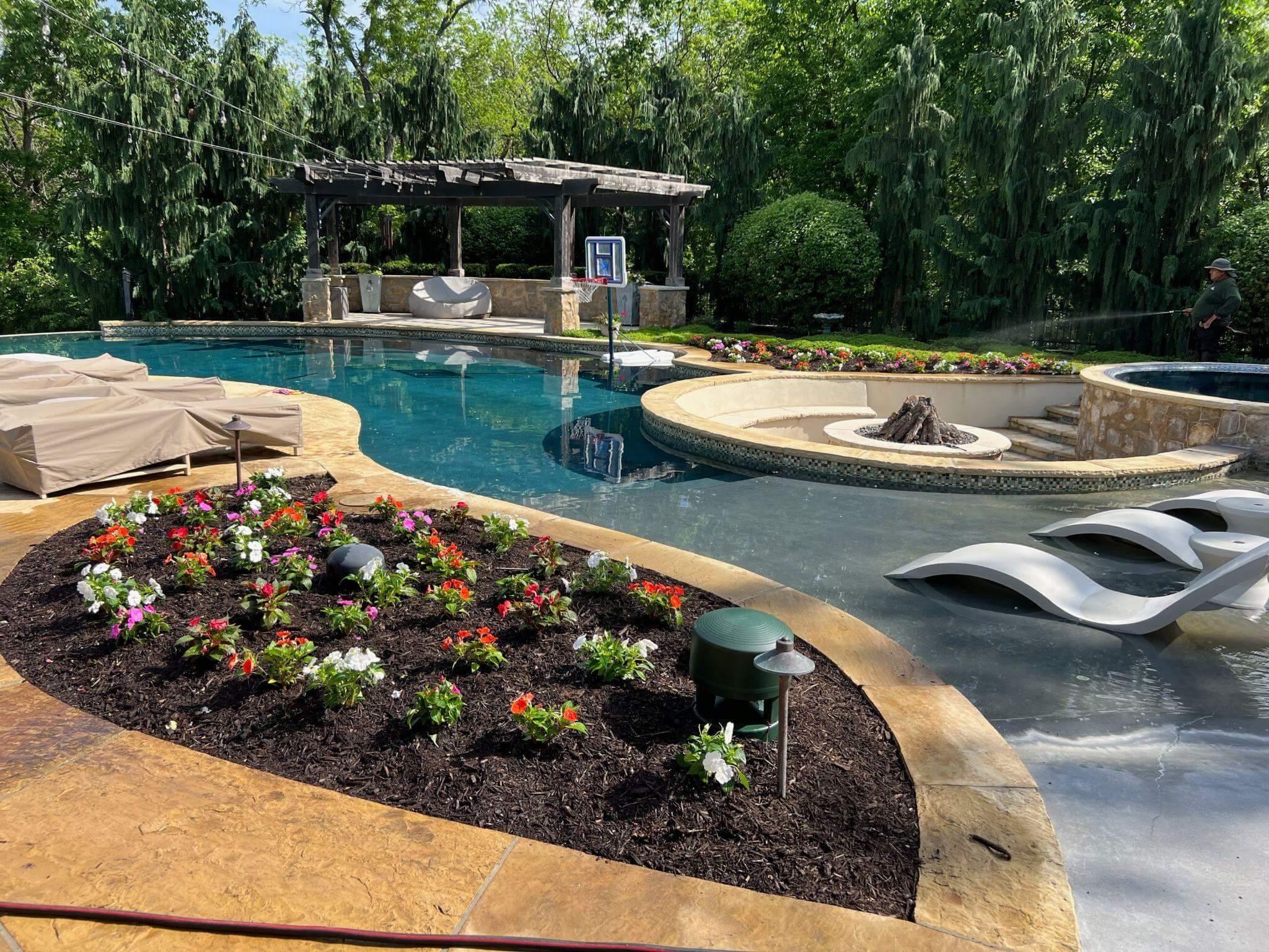 Luxury backyard with custom swimming pool, pergola, fire feature, landscape lighting, and colorful flower beds.
