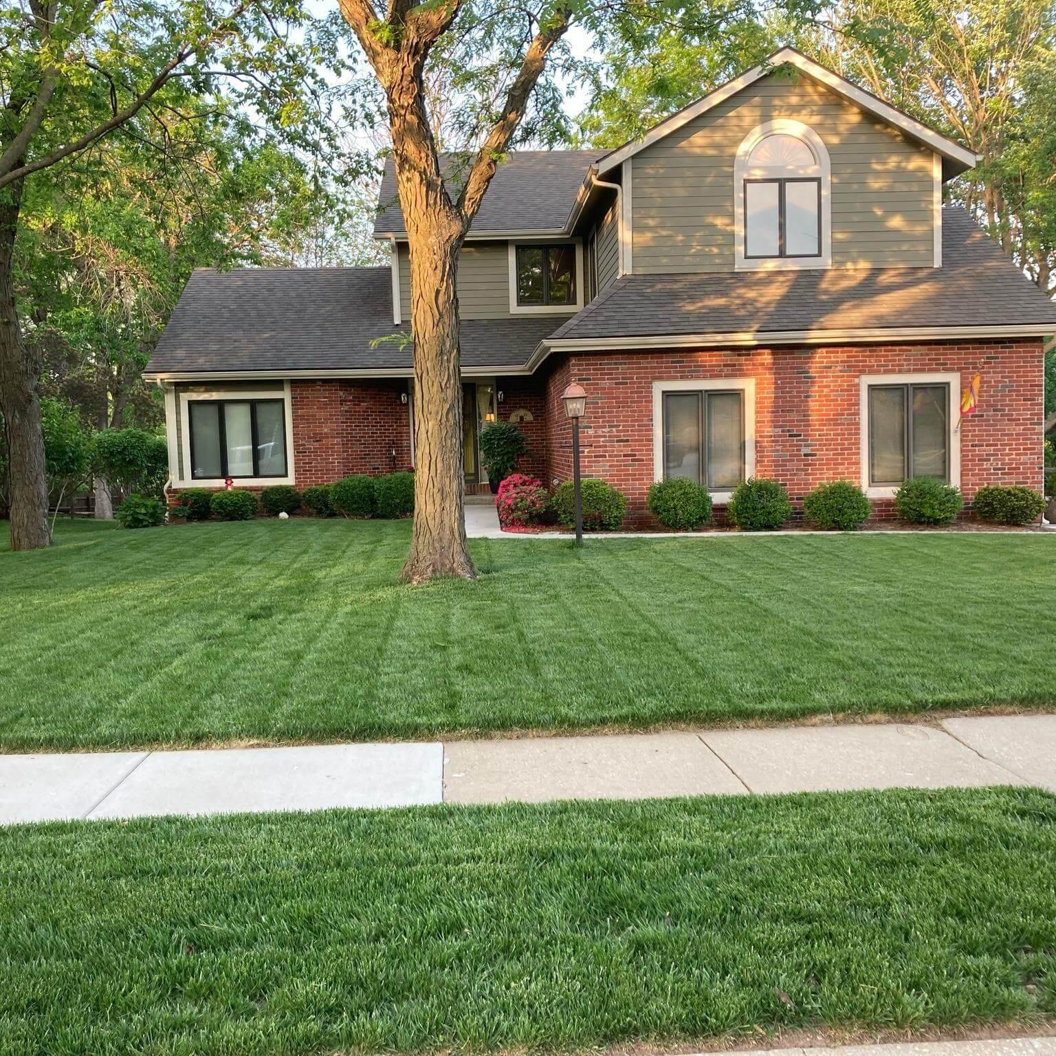 Well-maintained suburban home with striped green lawn and neatly trimmed foundation shrubs.